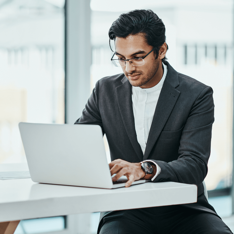 A man sits at a table while working on a laptop device.