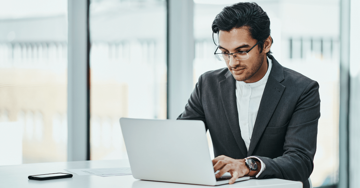 A man sits at a table while working on a laptop device.